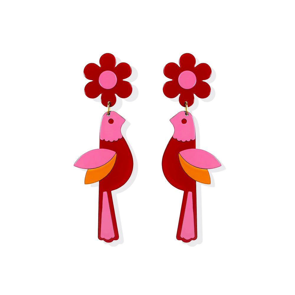 A pair of red bird-shaped earrings with pink flower tops and orange-pink wings, shown against a grey background – a playful sculptural design by ISUWA.

