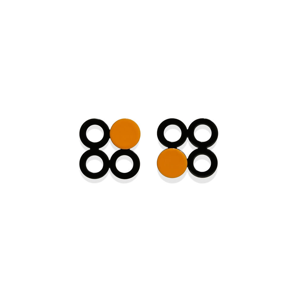 A pair of small orange and black dot earrings featuring four black circular shapes and one bold orange circle. Glossy finish, displayed on a white background with graphic symmetry.
