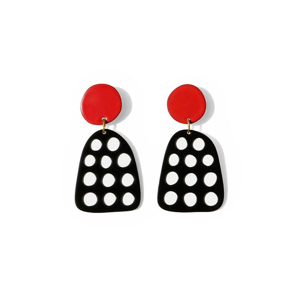 Pair of black statement earrings with circular cut-out dots and red round tops, placed on white background.