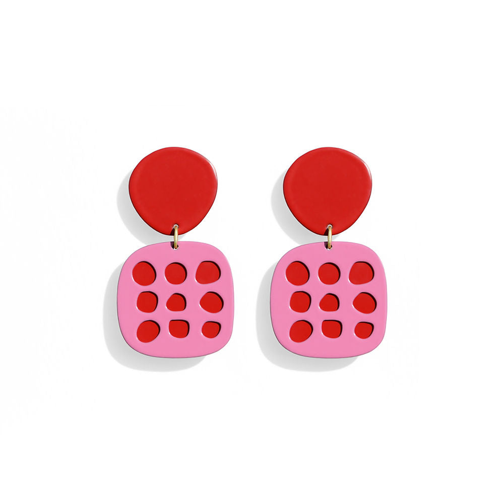 Pair of pink earrings with red circular cut-outs arranged in a grid, topped with red rounded studs, displayed on a white background.
