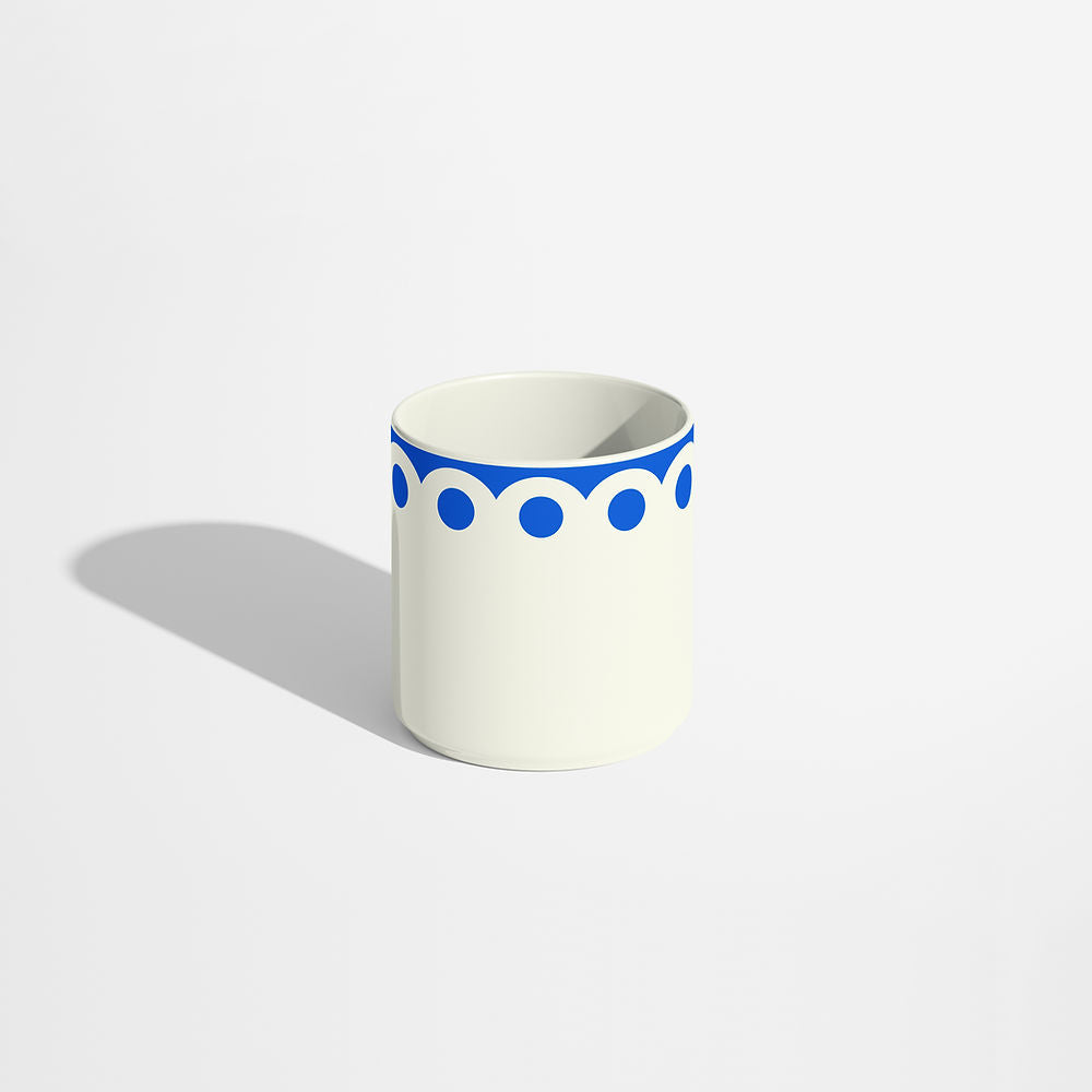 Blue porcelain coffee cup with bold circular dot pattern along the top edge, photographed on a white background with soft natural shadows.
