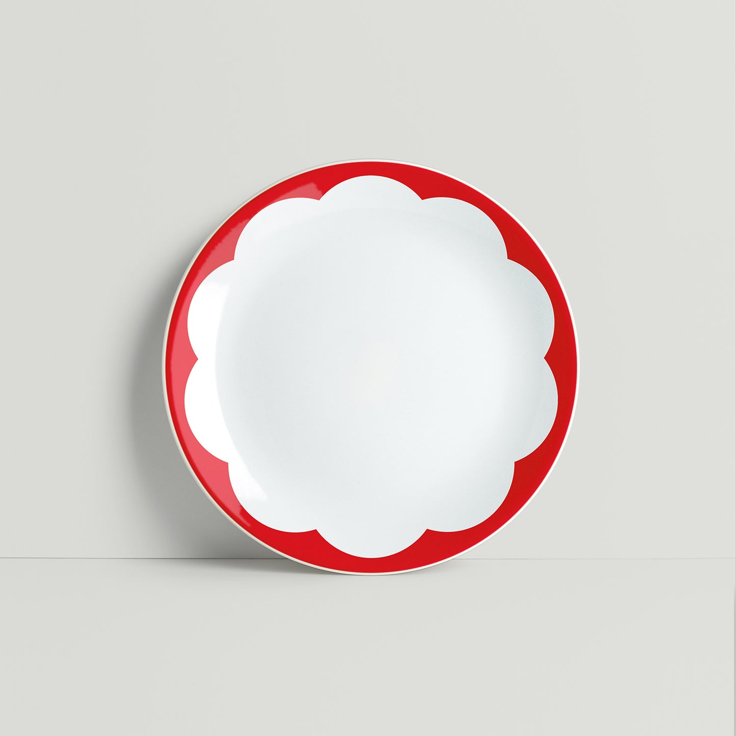 Red daisy-shaped porcelain plate with bold petal design, displayed on a light background.
