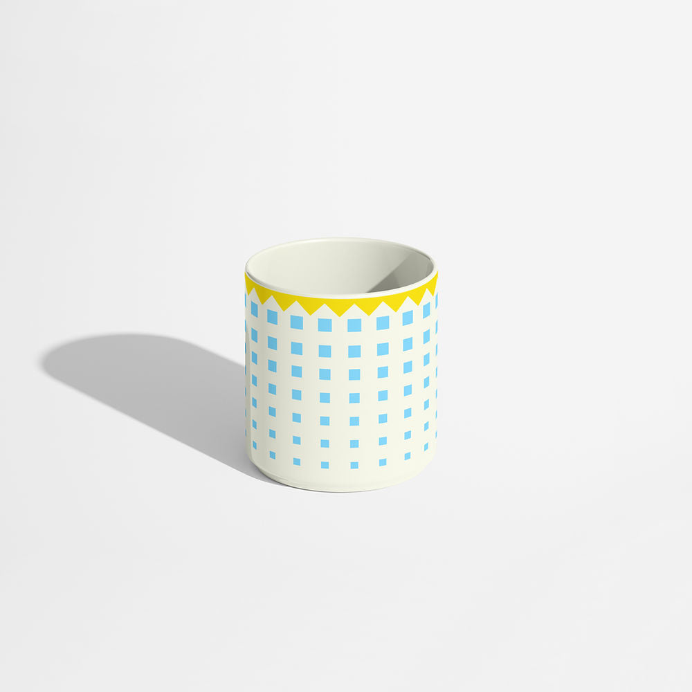 Blue and yellow porcelain coffee cup featuring a geometric grid of light blue squares and a yellow zigzag border, styled on a white background.
