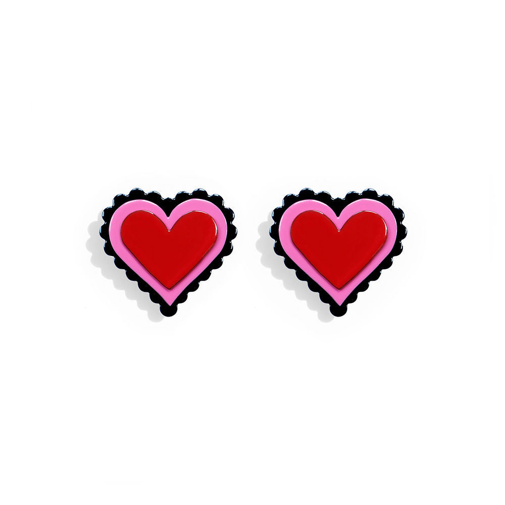 Heart-shaped earrings in red with pink and black scalloped edges, designed by ISUWA in a bold sculptural pop-art style, photographed on a white background.
