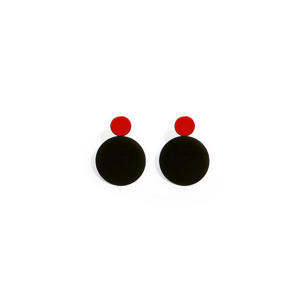 Pair of Luna Earrings featuring a red dot above a black disc, creating a graphic and sculptural circle design, displayed on a white background.