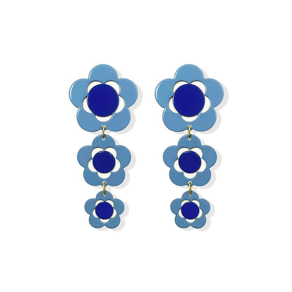 A pair of sculptural flower earrings featuring layered blue pansy shapes with dark blue centers. Glossy finish and dangling floral elements, displayed on a white background.
