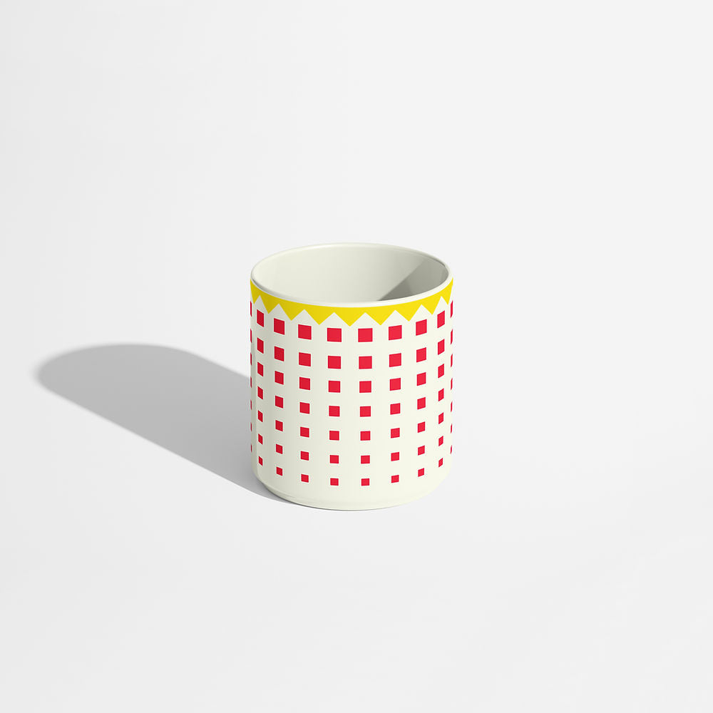 Porcelain coffee cup with a bold red square pattern and yellow zigzag rim on an ivory background.
