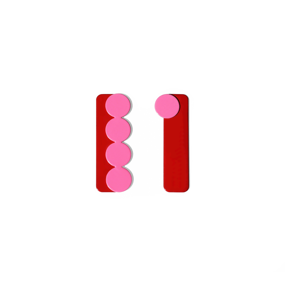 A pair of asymmetrical earrings featuring red vertical bars with pink circular accents. One earring has four pink circles aligned vertically, while the other has a single pink circle at the top. Bold and minimalist design, photographed on a white background.
