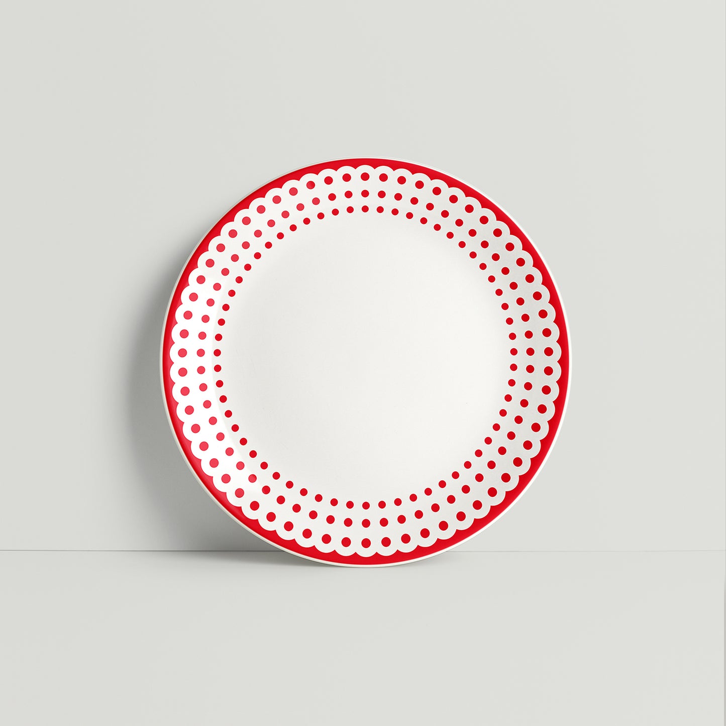 Round white porcelain plate with bold red dotted border, displayed against a neutral background, showcasing its playful and modern design.
