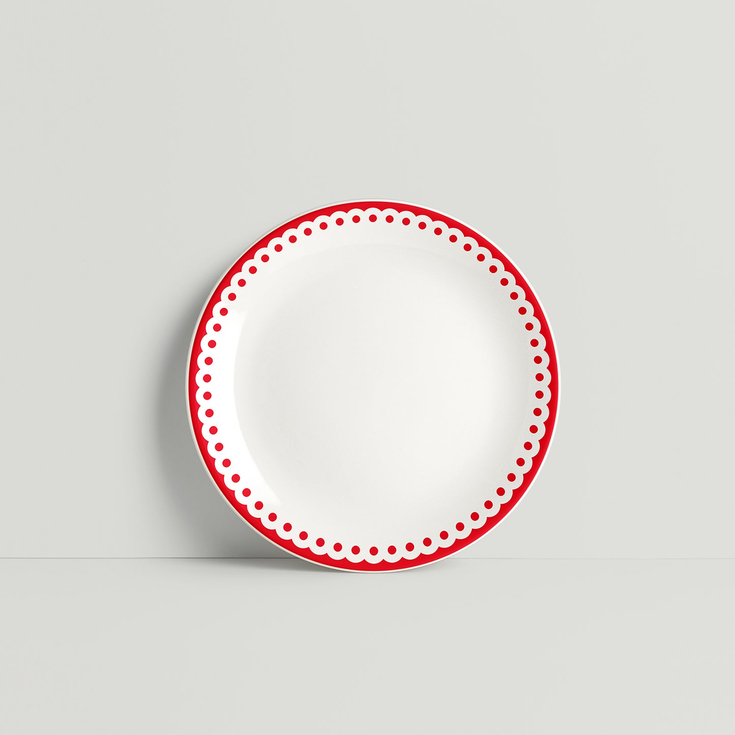 Top view of ISUWA’s red porcelain plate with a dotted pattern along the rim, styled on a minimal grey background
