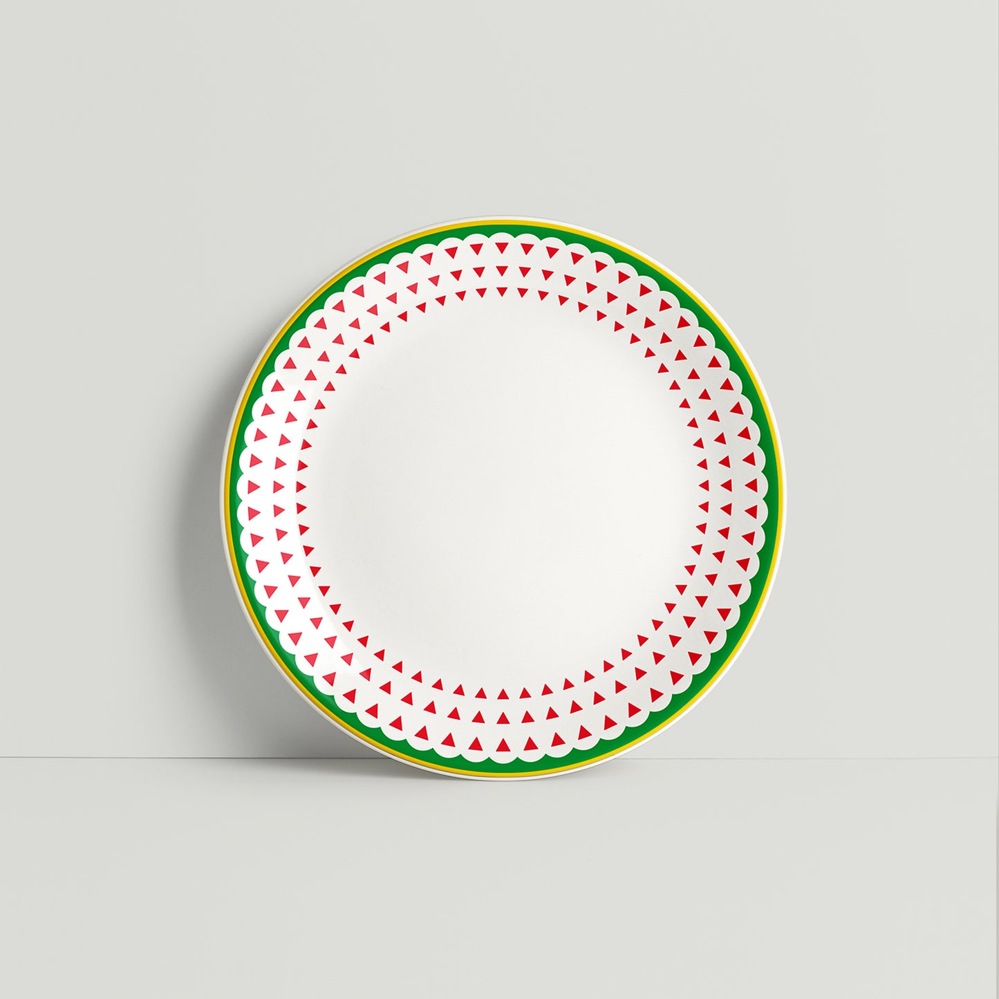 Round porcelain plate with red triangle pattern and green border on a white background.
