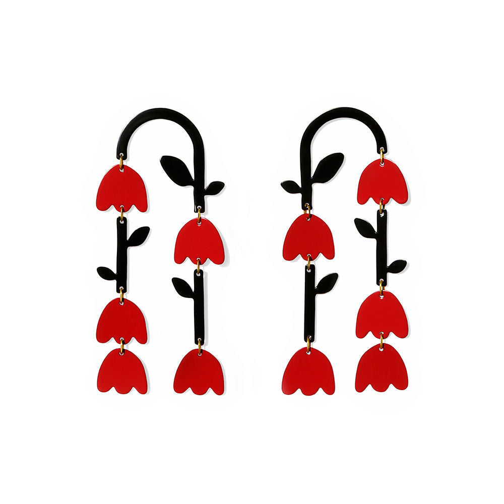 A pair of bold statement earrings shaped like stylized flower stems. Each earring features a curved black stem with black leaves and three hanging red tulip-shaped blossoms. Playful and graphic floral design on a white background.
