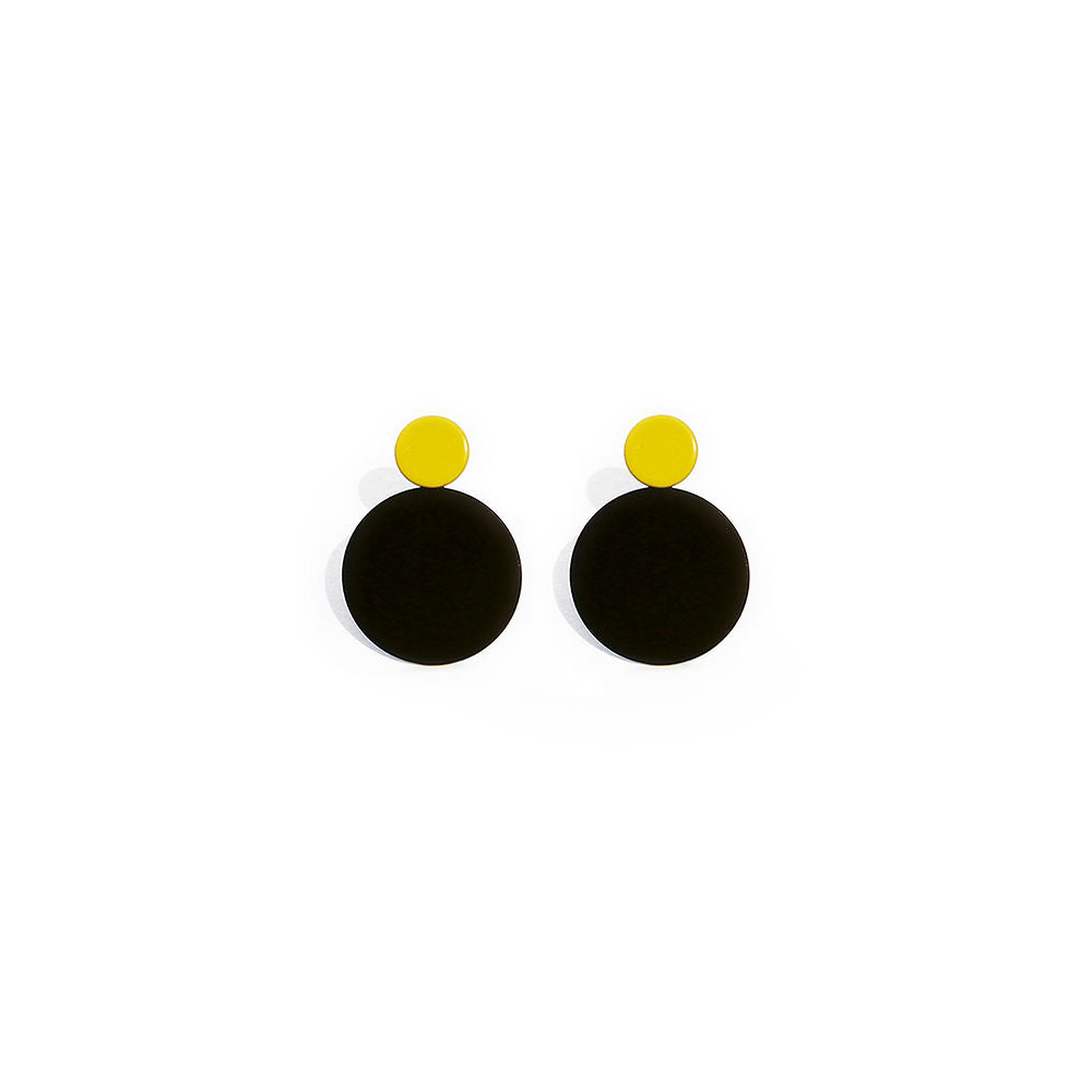A pair of sculptural earrings with glossy black circular bases and small yellow studs. Bold and minimal design, displayed on a clean white background.
