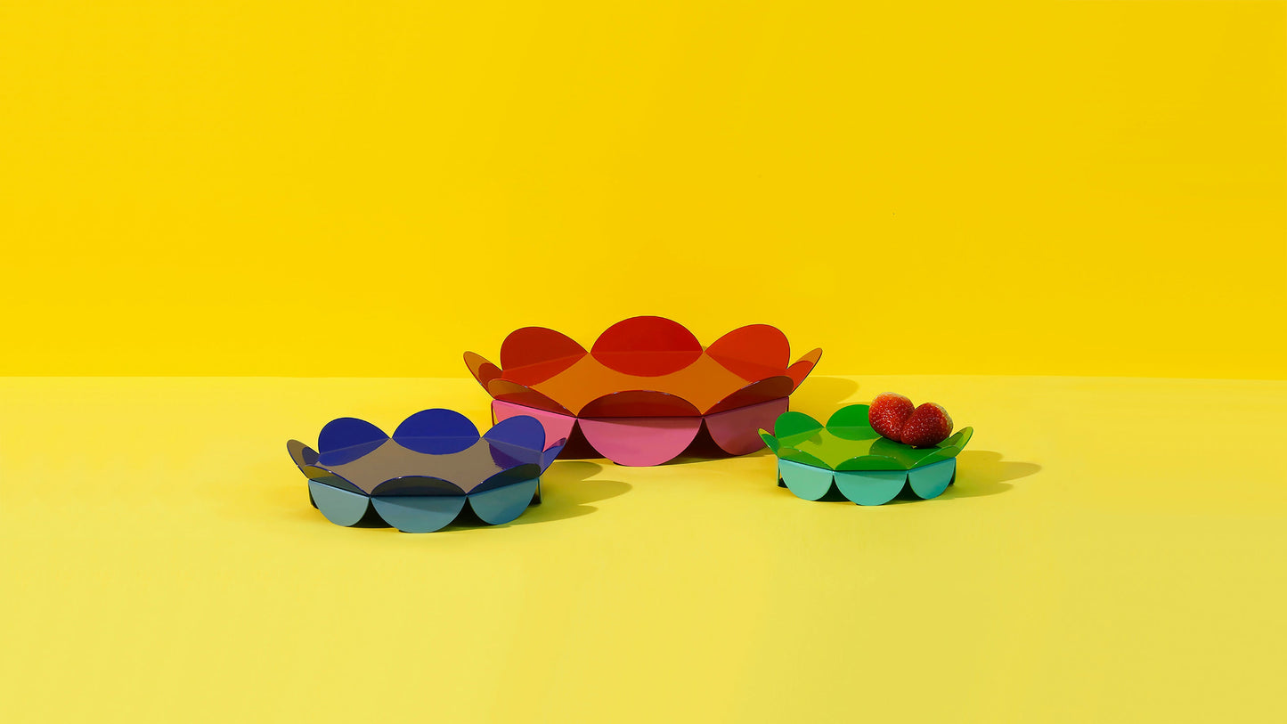 ISUWA Sculptural Flower Serving Stands – artistic metal serving bowls in blue, red and green with bold floral wave shapes, displayed on a vibrant yellow background.