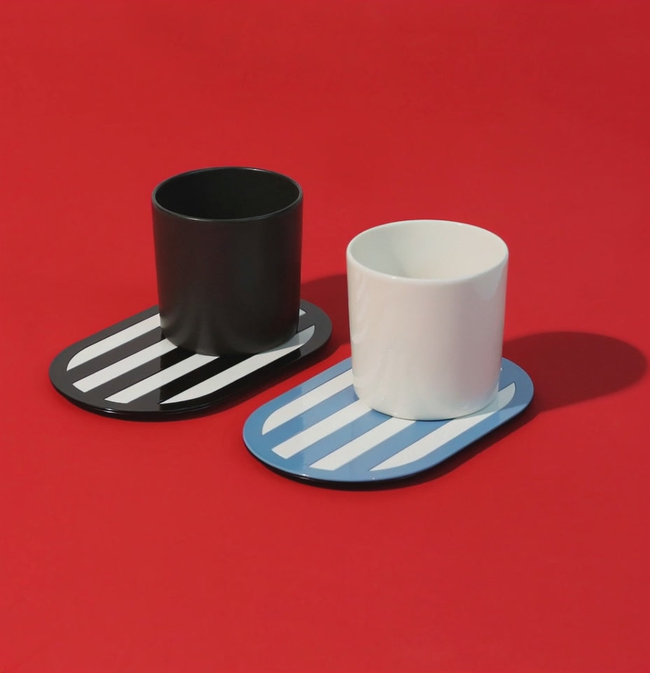 A close-up video of three glossy, colorful coasters on a vibrant surface. The camera starts with an overhead view and slowly shifts to a side angle, showcasing the modern shapes and shiny finish under soft studio lighting.