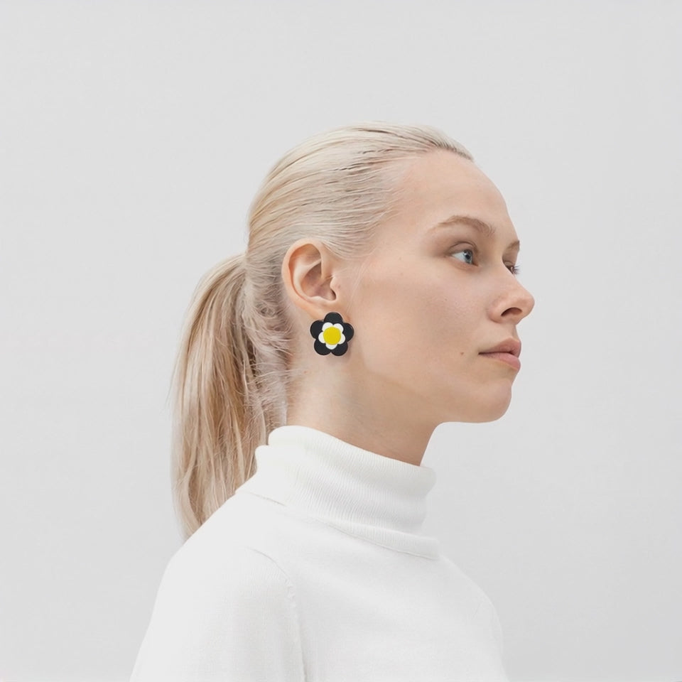 360-degree video showing a model wearing ISUWA’s black pansy earrings with white petals and a yellow center, highlighting their sculptural design and glossy finish in motion.

